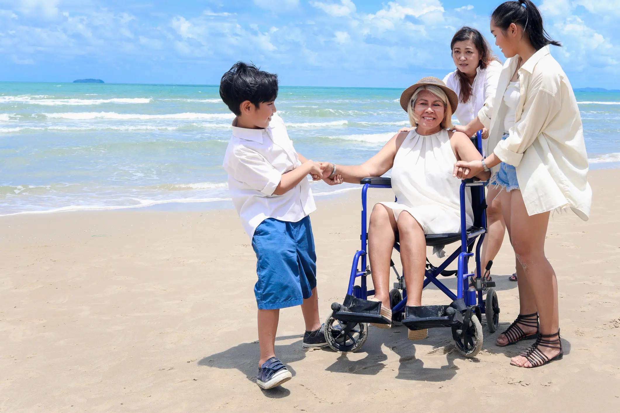 Happy disabled senior elderly woman in wheelchair spending time together with her family on tropical beach. Asian grandma, daughter and grandchildren resting and relaxing on summer holiday vacation. Happy disabled senior elderly woman in wheelchair spending time together with her family on tropical beach. Asian grandma, daughter and grandchildren resting and relaxing on summer holiday vacation.